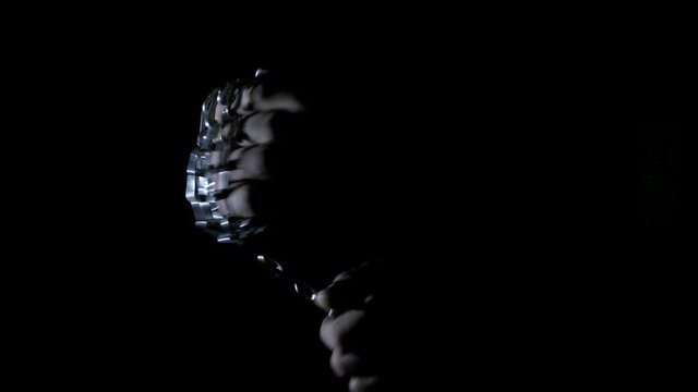 A man reels a chain around his fist for a fight. Black background.