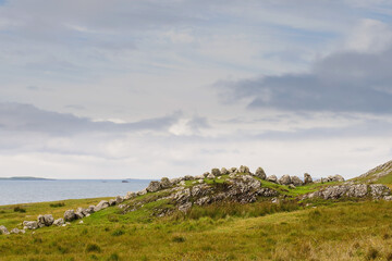 Fototapeta na wymiar Stones on a hill resemble sleeping dragon, Ocean and pastel blue cloudy sky in the background. Landscape scene in county Mayo, Ireland.