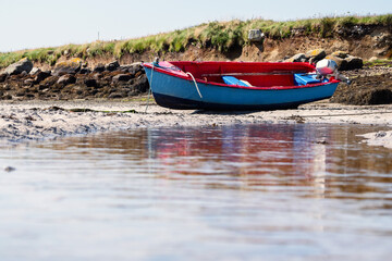 Small blue color fishing boat with red painted interior on a sandy beach at low tide. Food supply chain industry.