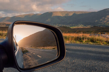 Road and sun rise view in a car mirror, stunning mountains out of focus in the background....
