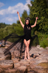Dance Ideas. Beautiful Caucasian Female Dancer in Black Light Dress Wearing Artistic Seashell Crown While Dancing On Rocky Seashore.