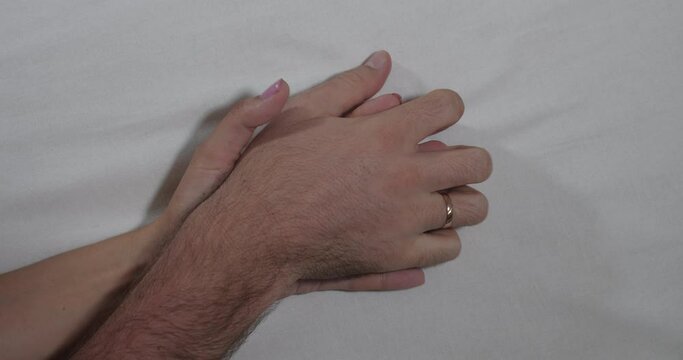 A close-up of the hands of an unrecognizable man and woman making love on a white sheet. Romance and humiliation concept