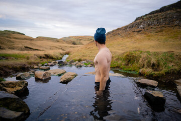 Man relaxing in a small geothermal hot spring pool in Hrunalaug, Iceland - obrazy, fototapety, plakaty