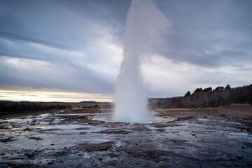 Eruption of Strokkur geyser in Iceland. Winter cold colors, sun lighting through the steam