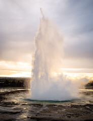 Eruption of Strokkur geyser in Iceland. Winter cold colors, sun lighting through the steam