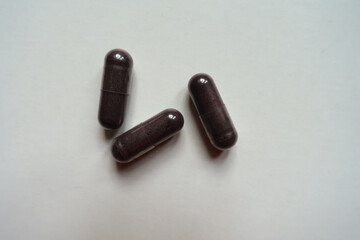 Three dark purple capsules of bilberry extract dietary supplement