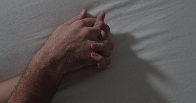 A close-up of the hands of an unrecognizable man and woman making love on a white sheet. Romance and humiliation concept
