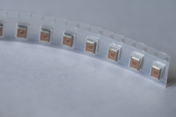 Extreme Closeup of Tape with SMD or Surface Mount Inductance Components in Tape Together On White.