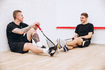 Full-length portrait of two sportive boys, squash players resting after productive team game