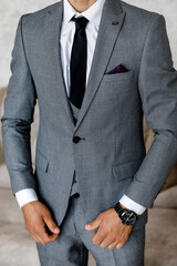 a man in a gray trouser suit three-piece with a white shirt and black tie in a watch and with a purple handkerchief