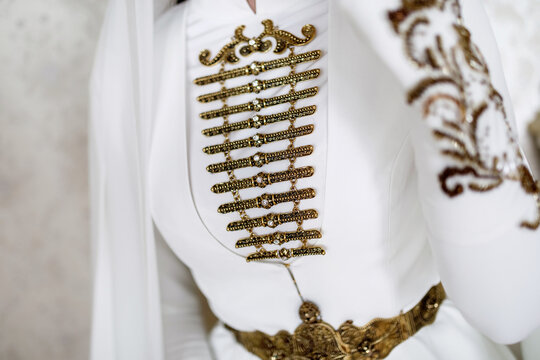 gold metal decoration of the national Caucasian wedding dress of a young girl on a light background