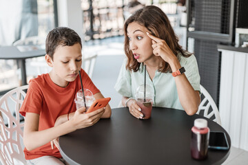 Emotional conflict between mother and son about smartphone addiction in cafe. An angry mom and a...
