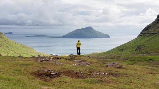 Aerial view of unrecognizable man looking at the panorama, islands, ocean, green mountain and rock cliffs.Impressions of the fascinating archipelago of the Faroe Islands in the North Atlantic Ocean