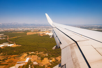The wing of an airplane flying over mountains and forests. Travel and air transport