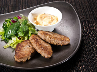 portion of beef rissoles on a plate served with salad mix and sauce thousand island, photo on dark background