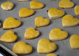 a lot of heart-shaped cottage cheese cookies, smeared with orange-yellow john on top, lie on parchment paper after baking in the oven. gluten-free homemade cakes. heart