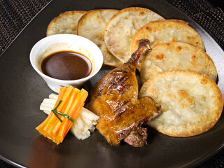 fried duck leg on a plate served with crispy croutons, carrot, celery and spicy sauce, photo on dark background