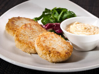 portion of chicken patties on a plate served with salad mix and sauce thousand island, photo on dark background