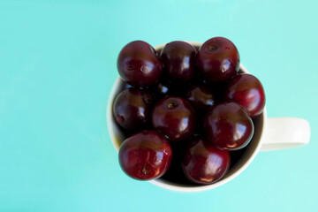 close-up of a lot of red juicy cherries in a white cup on a turquoise background top view. ripe summer berries