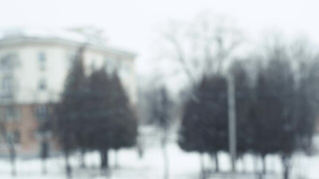 Snow falls in winter against blurred cityscape. Defocus t house and tree