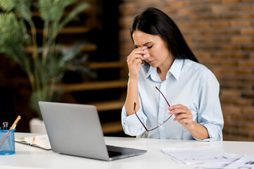 Headache and migraine. Exhausted caucasian young adult woman, top manager, office employee, tired of works, in stress, took a break from work, need a rest, massages the bridge of her nose, closes eyes