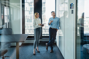 Male professional discussing over white board with female colleague while planning strategy in office