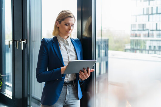 Businesswoman using digital tablet while standing by glass window in office