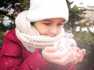 The girl admires the Christmas tree toy. Winter holidays. Child rejoices at Christmas. The child...