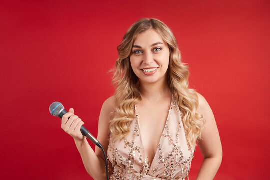 Smiling singer in a beautiful dress with a microphone posing on a red background