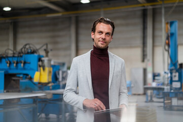 Businessman in gray blazer standing with digital tablet in factory