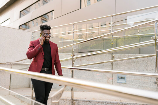 Smiling Male Professional Talking On Mobile Phone While Walking By Railing