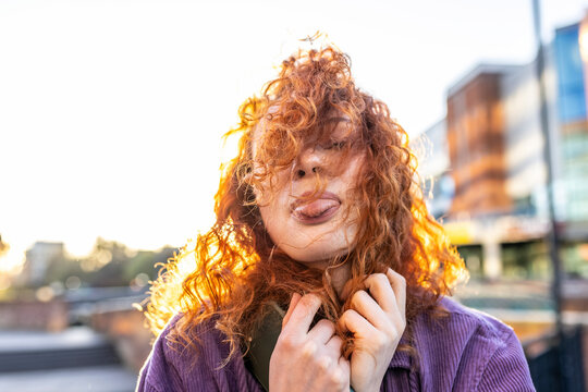 Curly haired woman sticking out tongue during sunset