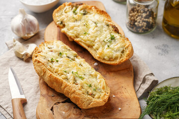Two halves of garlic and butter bread - baguette on a wooden board, sea salt, pepper, dill and garlic cloves on a grey concrete background, top view