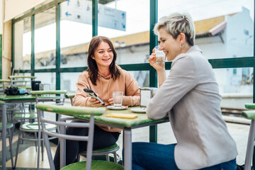 Two women chatting and showing something on the phone in the cafe at train station