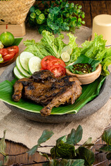 Ayam bakar or roasted chicken on banana leaf shoot at a rustic wooden background. Ayam bakar is a indonesian dish. Ayam bakar literally means 