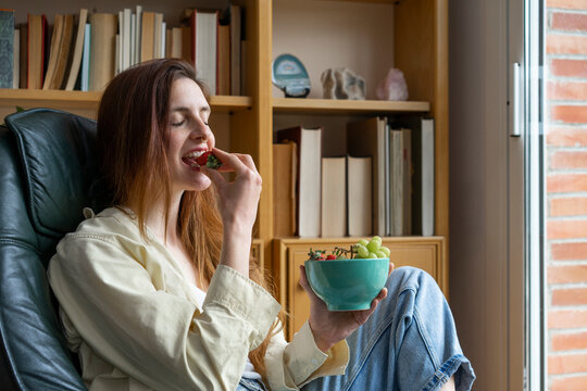 Beautiful Woman Eating Fruits While Sitting On Chair At Home