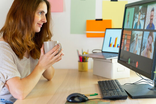 Female freelancer holding mug during video call on computer at home office