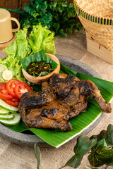 Ayam bakar or roasted chicken on banana leaf shoot at a rustic wooden background. Ayam bakar is a indonesian dish. Ayam bakar literally means 