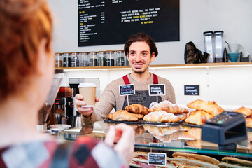 Smiling male owner offering coffee to female customer in cafe