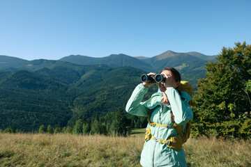 Tourist with hiking equipment looking through binoculars in mountains