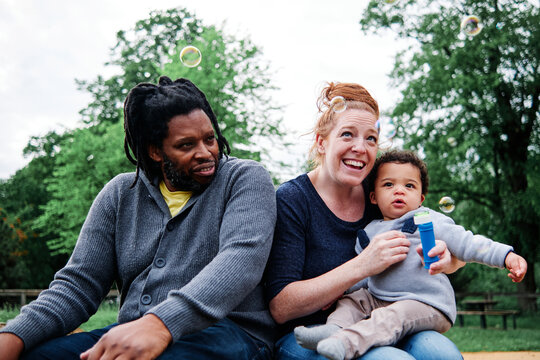 Mother looking away with son while playing with bubbles at park