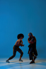 Couple dancing hip hop on blue backdrop in studio