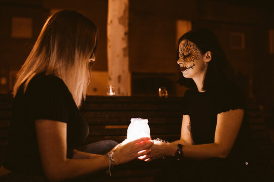 Female friends sitting with illuminated jar on bench during Halloween