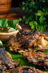 Ayam bakar or roasted chicken on banana leaf shoot at a rustic wooden background. Ayam bakar is a indonesian dish. Ayam bakar literally means 