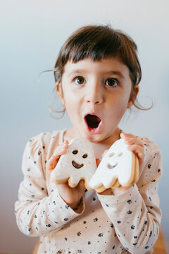 Cute girl with mouth open holding ghost cookies