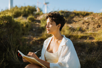 Thoughtful woman sitting with notebook on sunny day