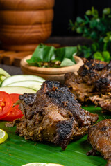 Ayam bakar or roasted chicken on banana leaf shoot at a rustic wooden background. Ayam bakar is a indonesian dish. Ayam bakar literally means 