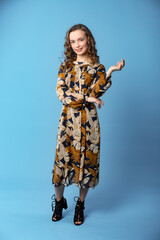 studio, beautiful woman. model on a blue background in a dark blue dress with a yellow floral armenite poses for the camera. model pose. beauty shooting, holiday