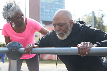 Senior woman motivating bald man exercising on railing at park