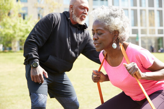 Woman with resistance band exercising by man on sunny day